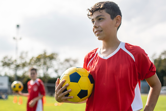 Un jugador de fútbol adolescente sostiene un balón mientras está en una cancha junto con su equipo. Este blog explica los riesgos del vapeo para los atletas adolescentes.